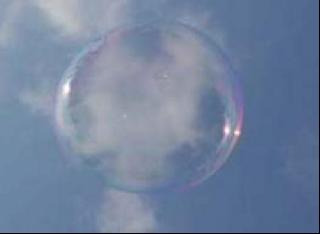 A transparent bubble photographed from below, before a blue and white sky.
