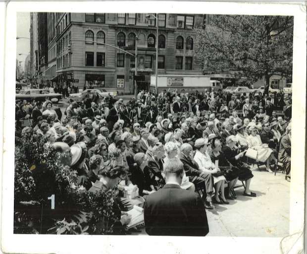 Old photo of a crowd watching a perfomance, with audience spread across the streets.