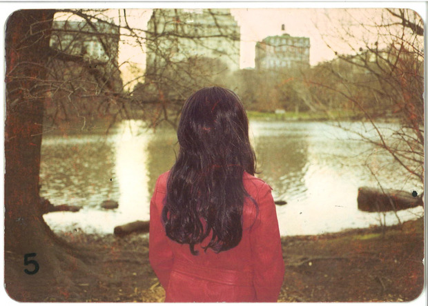 Woman in a red leather jacket looks out over Central Park lake with her back to the camera.