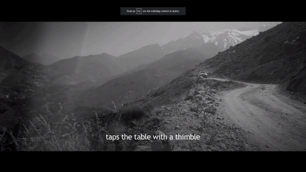 A movie frame of a black and white desert mountain landscape, with subtitles beneath in white.